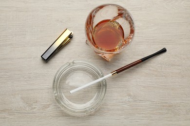 Photo of Glass ashtray with long cigarettes holder, lighter and alcohol drink on wooden table, flat lay