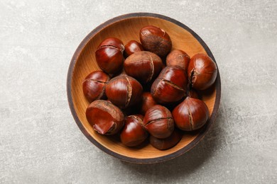Photo of Fresh edible sweet chestnuts in wooden bowl on grey table, top view