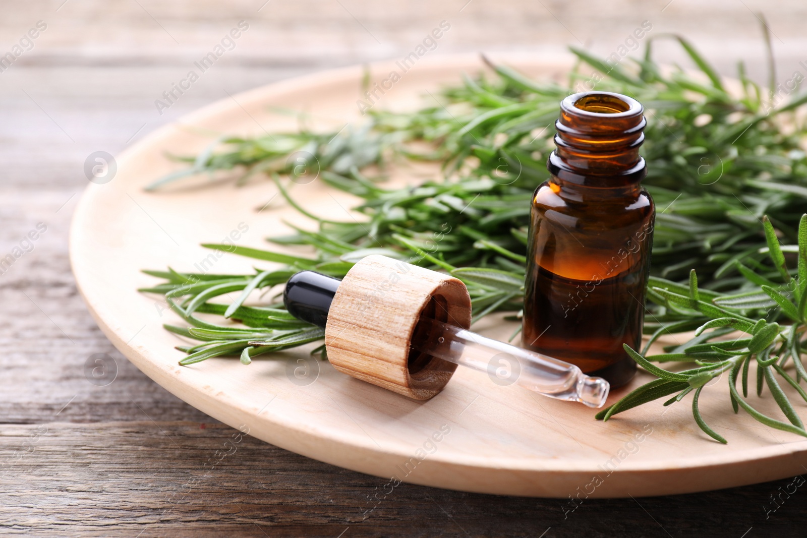 Photo of Bottle of rosemary essential oil and pipette on wooden table, closeup