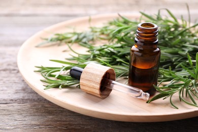 Bottle of rosemary essential oil and pipette on wooden table, closeup