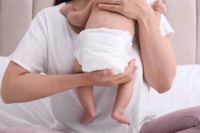 Mom holding her baby in diaper at home, closeup