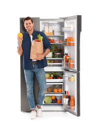 Man with bag of groceries near open refrigerator on white background