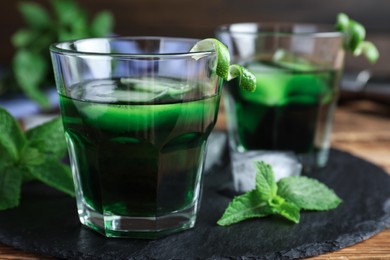 Photo of Delicious mint liqueur with green leaves on table, closeup