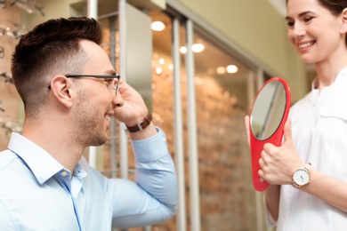 Female ophthalmologist helping man to choose glasses in optical store