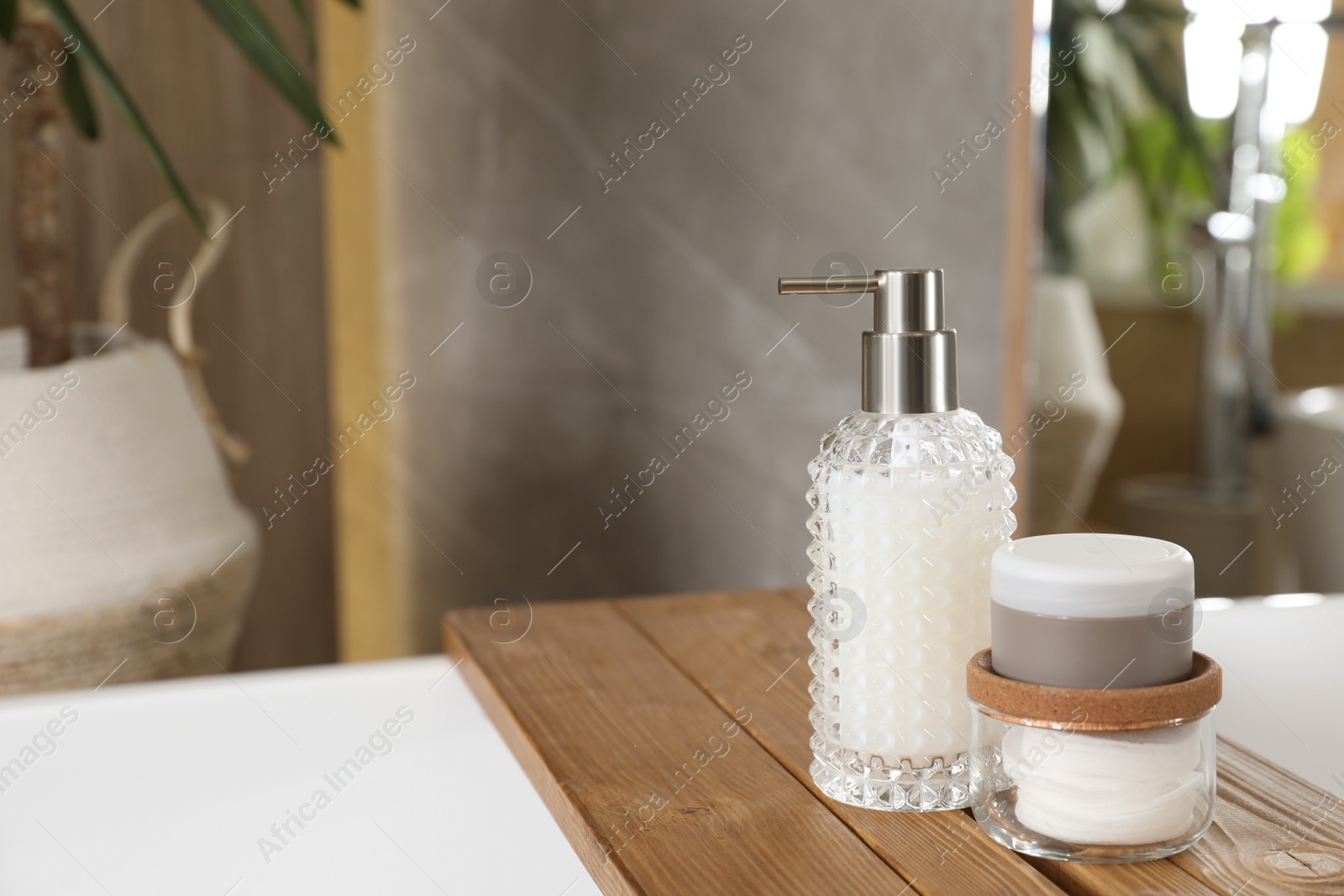 Photo of White tub with soap dispenser, cotton pads and jar in bathroom, space for text. Interior design