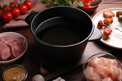 Photo of Fondue pot, forks with fried meat pieces and other products on wooden table