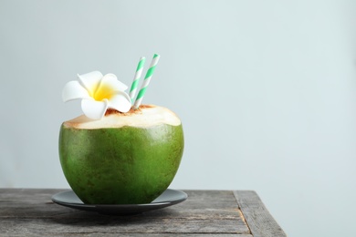 Fresh green coconut with drinking straws and flower on table against light background