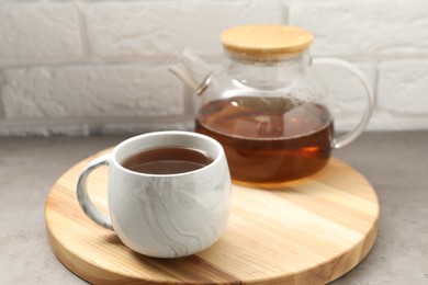 Photo of Aromatic tea in glass teapot and cup on gray table against white brick wall