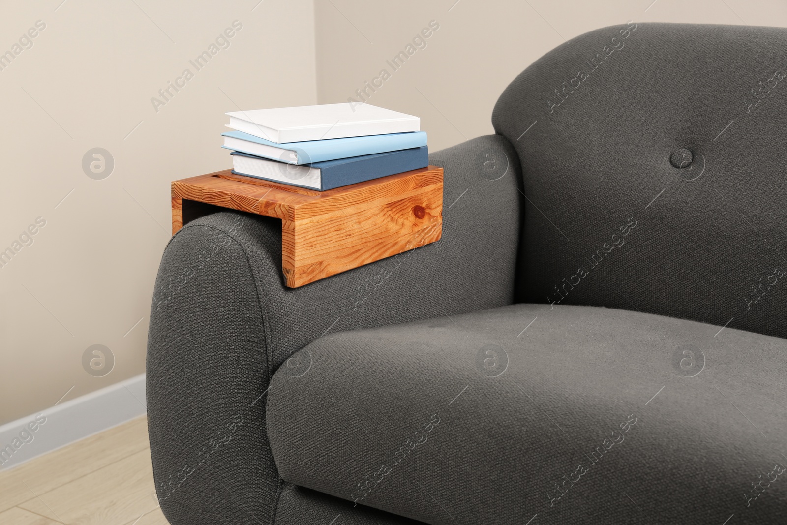 Photo of Books on sofa with wooden armrest table in room. Interior element