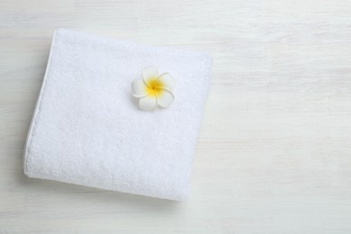 Photo of White terry towel and plumeria flower on light wooden table, top view. Space for text