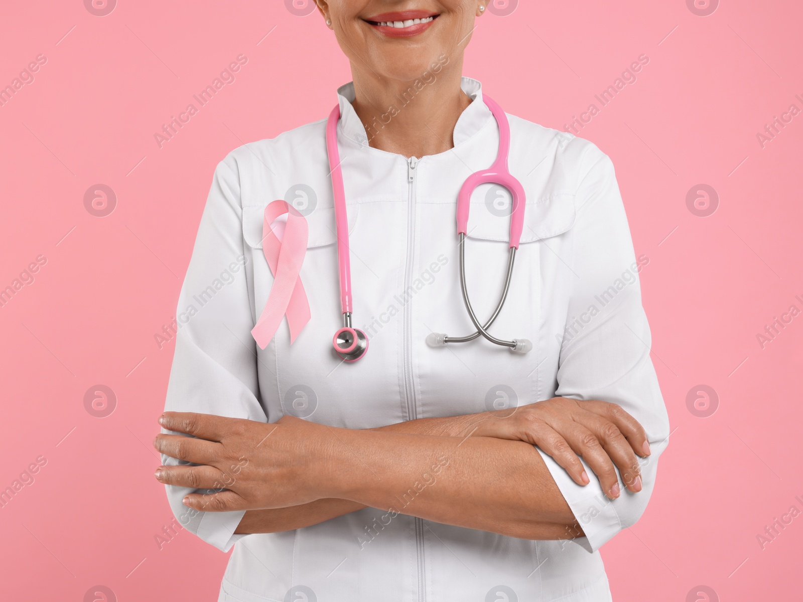 Photo of Doctor with pink ribbon and stethoscope on color background, closeup. Breast cancer awareness