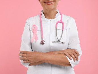 Photo of Doctor with pink ribbon and stethoscope on color background, closeup. Breast cancer awareness