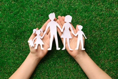 Photo of Woman holding family paper cutout on green grass, top view