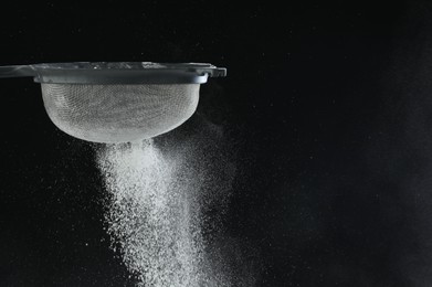 Woman sieving flour at table against black background, closeup