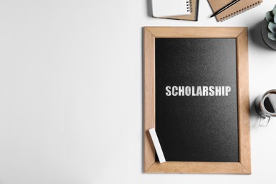 Image of Chalkboard with word SCHOLARSHIP and stationery on white table, flat lay. Space for text