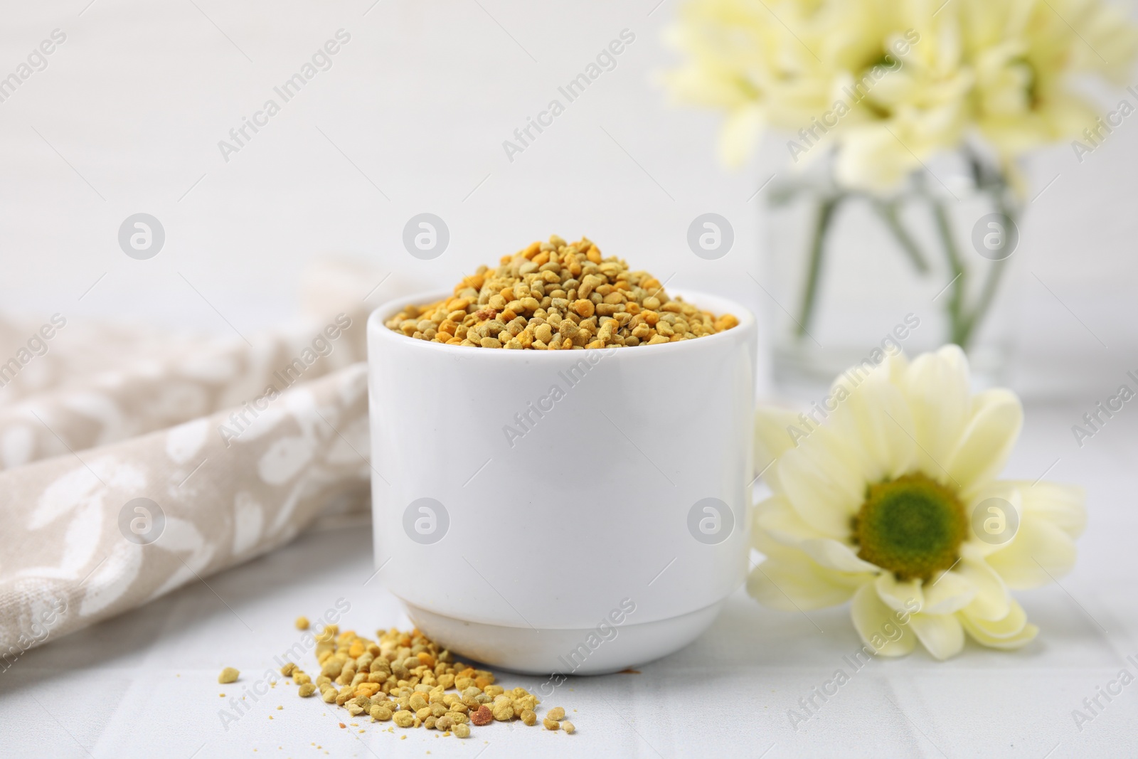 Photo of Fresh bee pollen granules and flower on white table