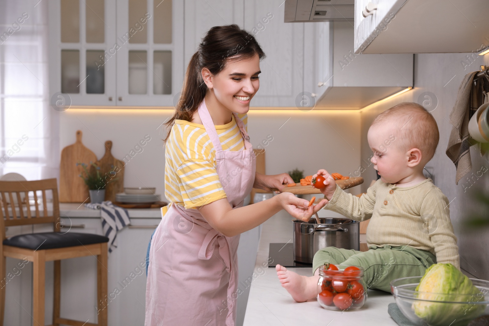 Photo of Happy young woman with her cute baby spending time together in kitchen