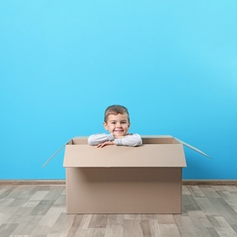Cute little boy playing with cardboard box near color wall