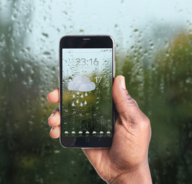 African-American man using weather forecast app on smartphone near window indoors, closeup