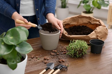 Woman filling flowerpot with soil at wooden table indoors, closeup. Transplanting houseplants