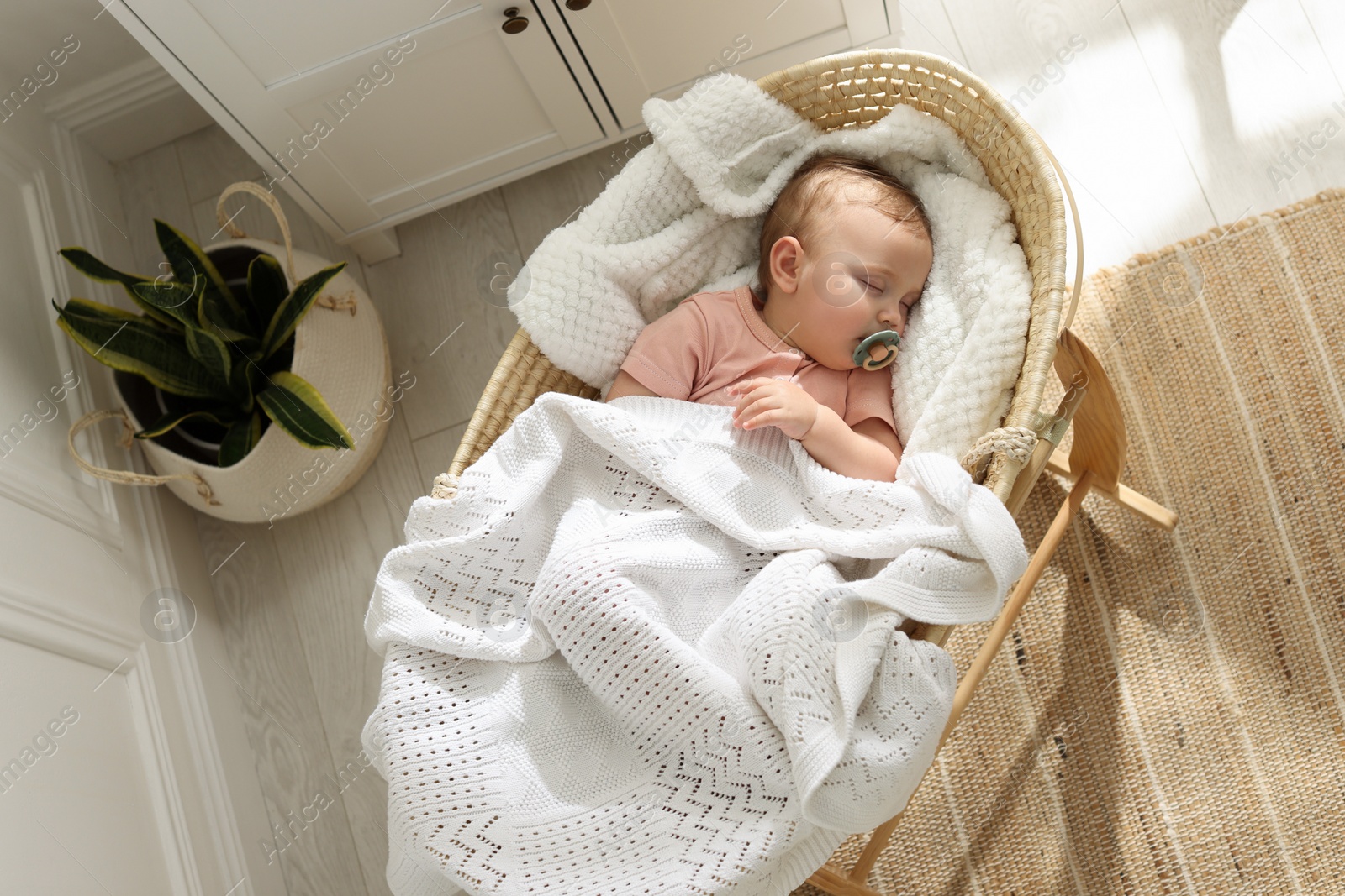 Photo of Cute little baby with pacifier sleeping in wicker crib at home, top view