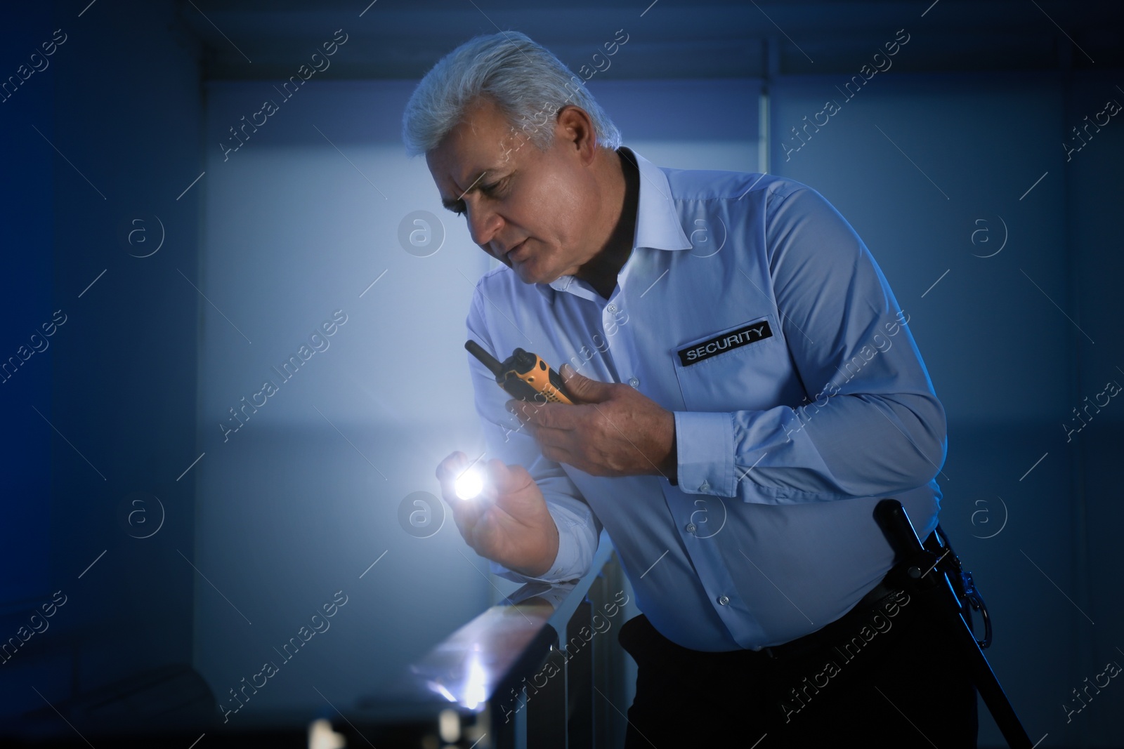 Photo of Professional security guard with portable radio set and flashlight in dark room