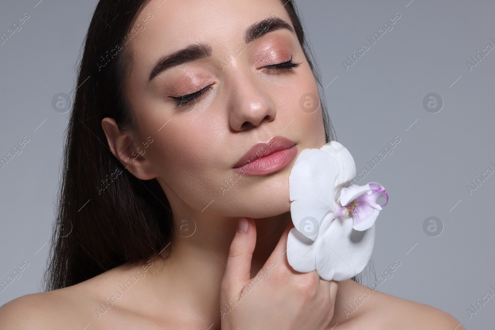 Photo of Portrait of beautiful young woman with orchid flower on grey background