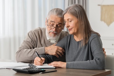 Photo of Elderly couple with papers discussing pension plan at wooden table indoors