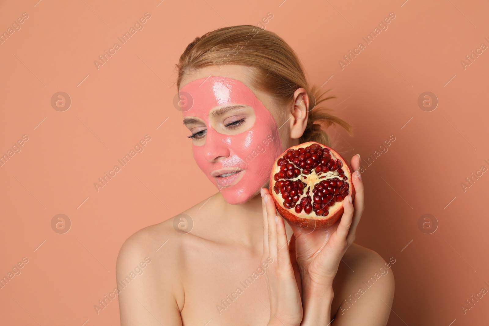 Photo of Young woman with pomegranate face mask and fresh fruit on pale coral background