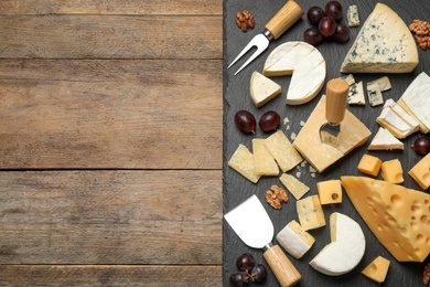 Photo of Cheese platter with specialized knives and fork on wooden table, top view. Space for text