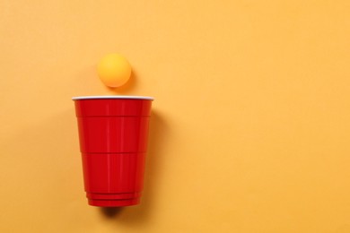 Photo of Plastic cup and ball on orange background, flat lay with space for text. Beer pong game