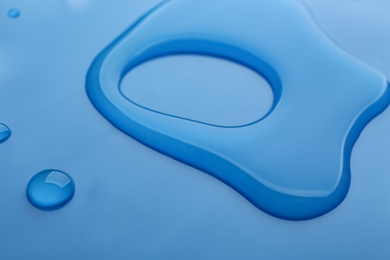 Photo of Drops of spilled water on blue background, closeup