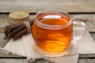 Photo of Aromatic licorice tea in cup and dried sticks of licorice root on wooden table, closeup