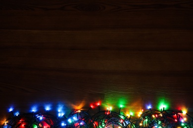 Photo of Colorful Christmas lights on wooden table, top view. Space for text