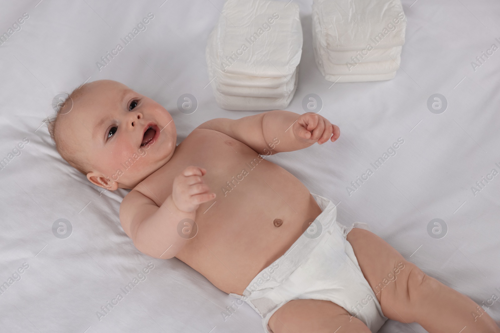 Photo of Cute little baby lying near stack of diapers on bed