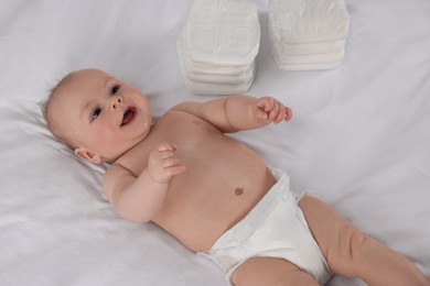 Photo of Cute little baby lying near stack of diapers on bed