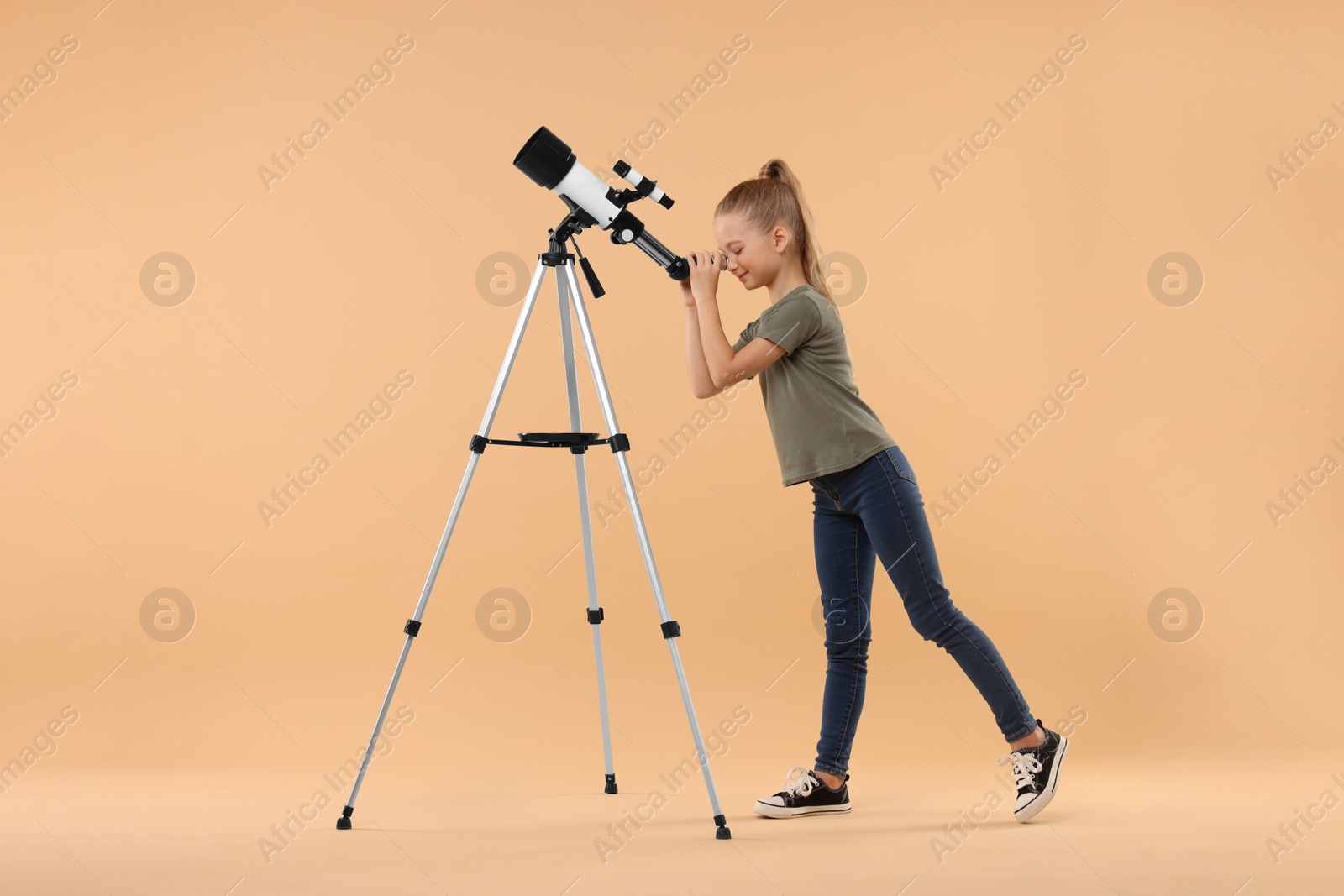 Photo of Little girl looking at stars through telescope on beige background