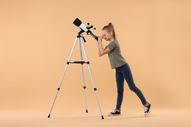 Photo of Little girl looking at stars through telescope on beige background