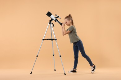 Little girl looking at stars through telescope on beige background