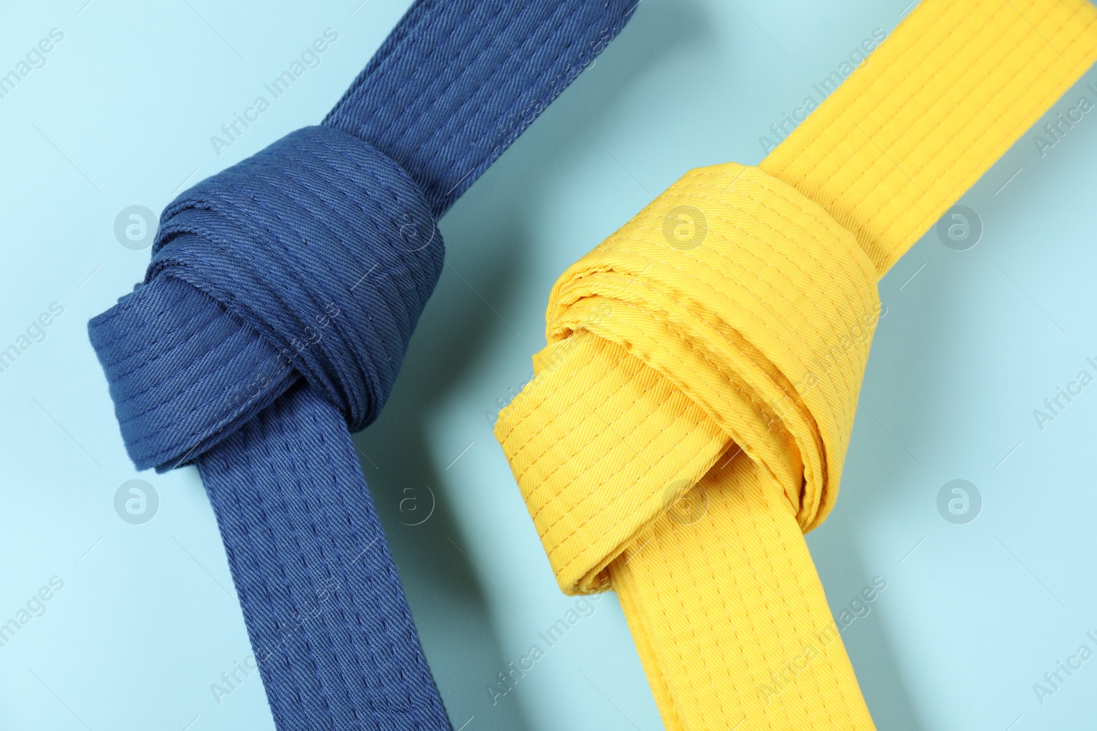 Photo of Colorful karate belts on light blue background, flat lay