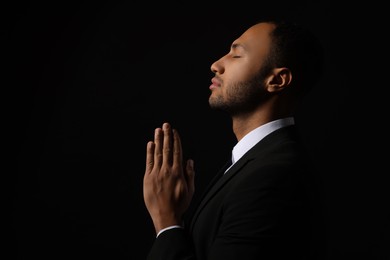 Photo of African American man with clasped hands praying to God on black background. Space for text