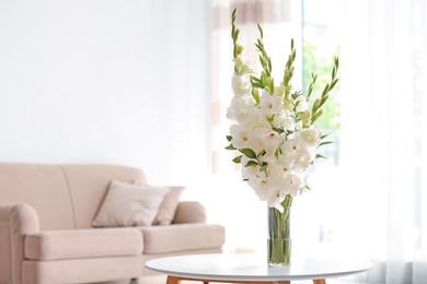 Photo of Vase with beautiful white gladiolus flowers on wooden table in living room. Space for text