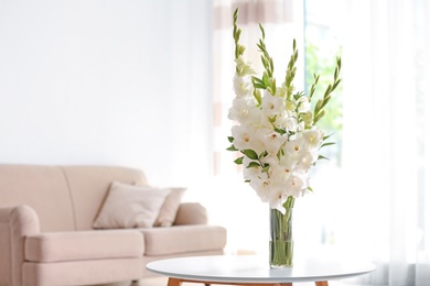 Vase with beautiful white gladiolus flowers on wooden table in living room. Space for text