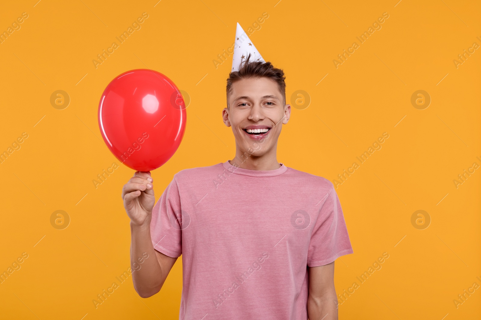 Photo of Happy man in party hat with balloon on orange background