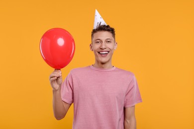 Photo of Happy man in party hat with balloon on orange background
