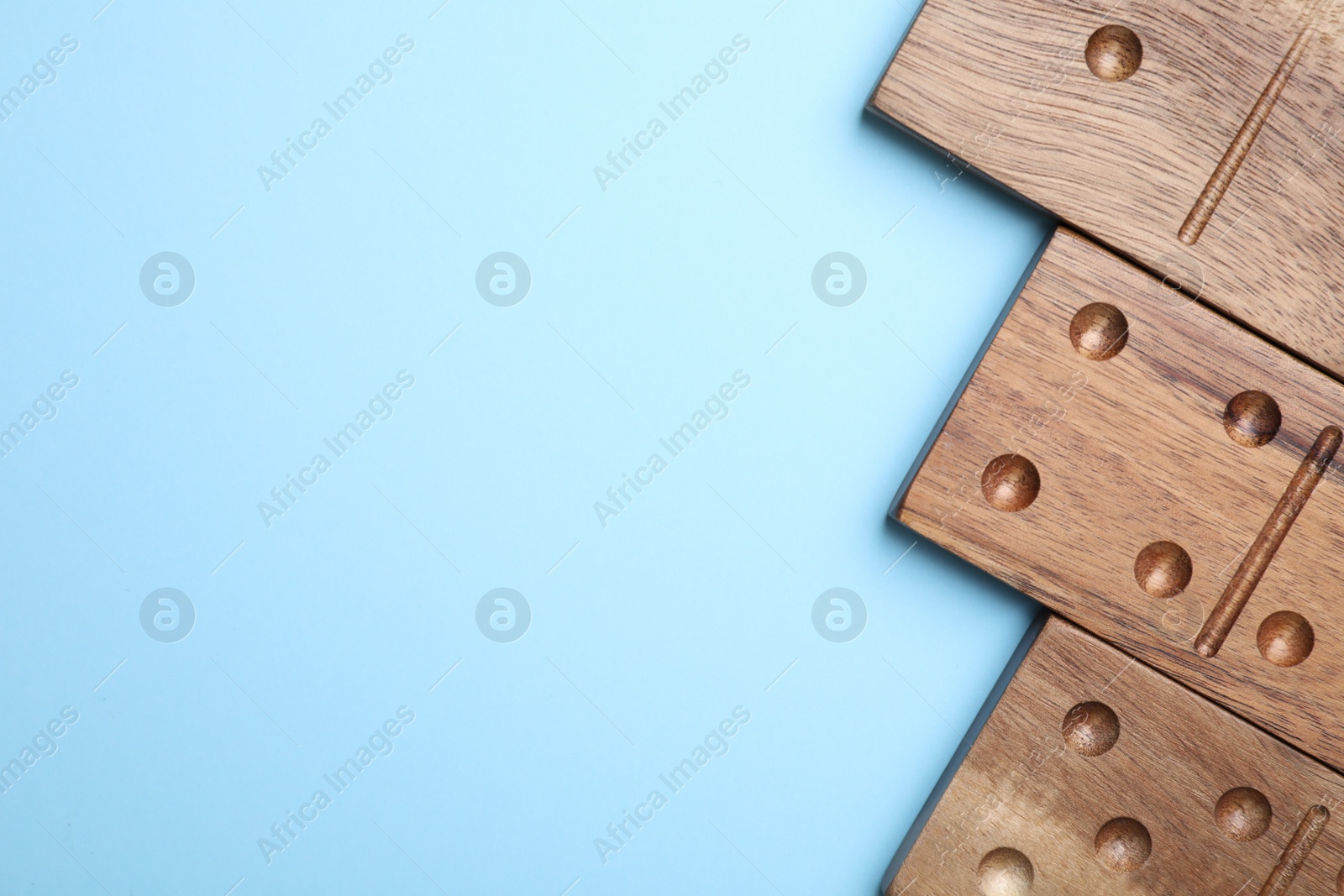 Photo of Wooden domino tiles on light blue background, flat lay. Space for text