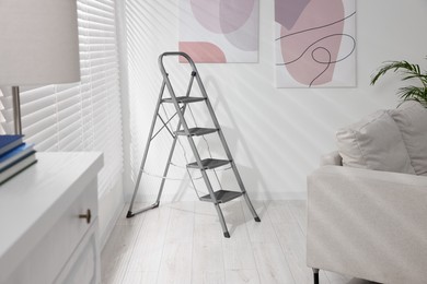 Photo of Metal ladder near window and abstract pictures in living room