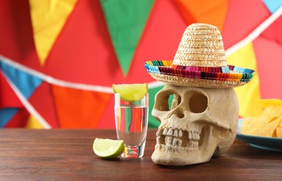 Human scull with Mexican sombrero hat and tequila on wooden table. Space for text