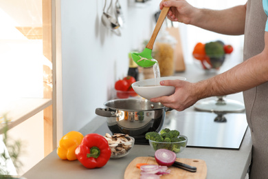 Young man pouring delicious soup into bowl at home, closeup