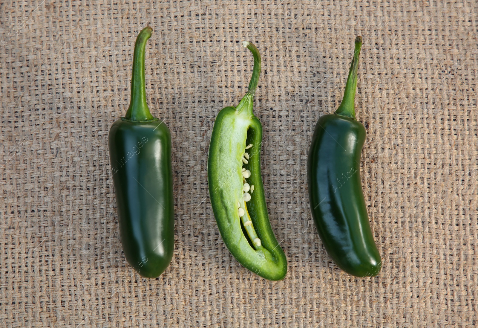 Photo of Whole and cut fresh green jalapeno peppers on sacking, flat lay